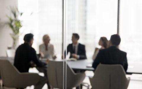 group of business professionals seated around a boardroom table behind frosted glass