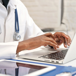 A medical professional types on a laptop