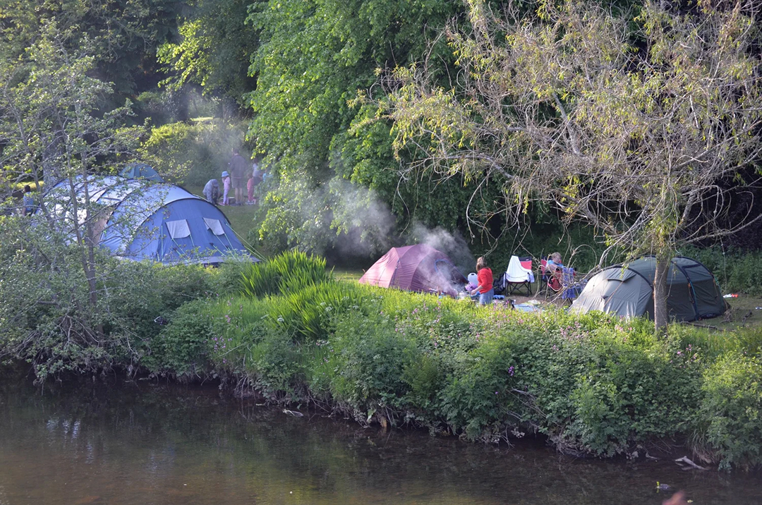 river-side camping area at penpont, number of tents shown and smoke from campfire