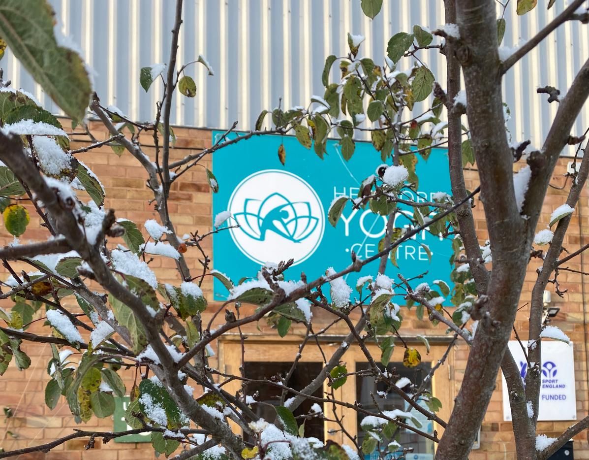 snowy image of Hereford Yoga Centre building with snowy branches in foreground and sign in background.