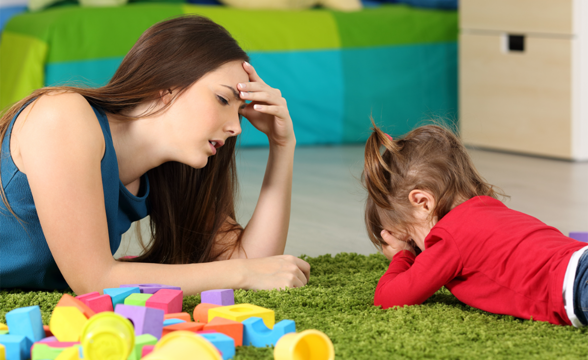 A frustrated mother laying on the floor with her young child