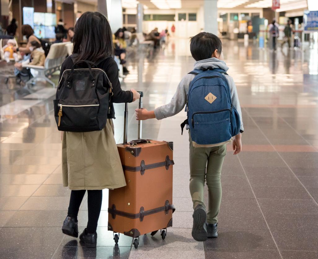 Two young children wheeling a suitcase at an airport
