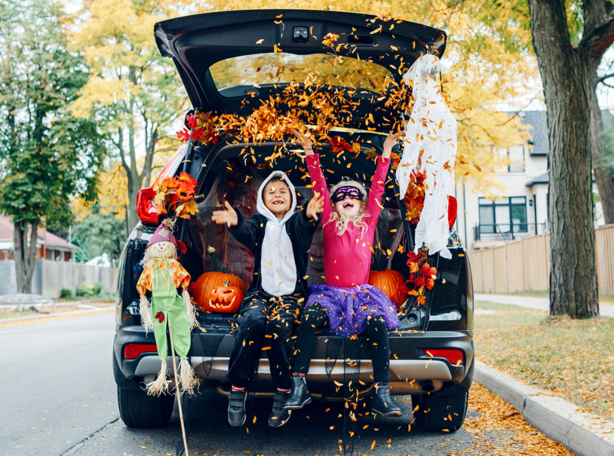 Children in costumes sitting in the trunk of a car decorated for Halloween