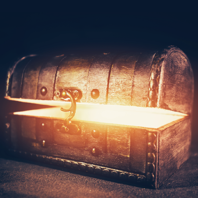 A close up of a wooden treasure box that is ajar. Golden light spills out from the opening.