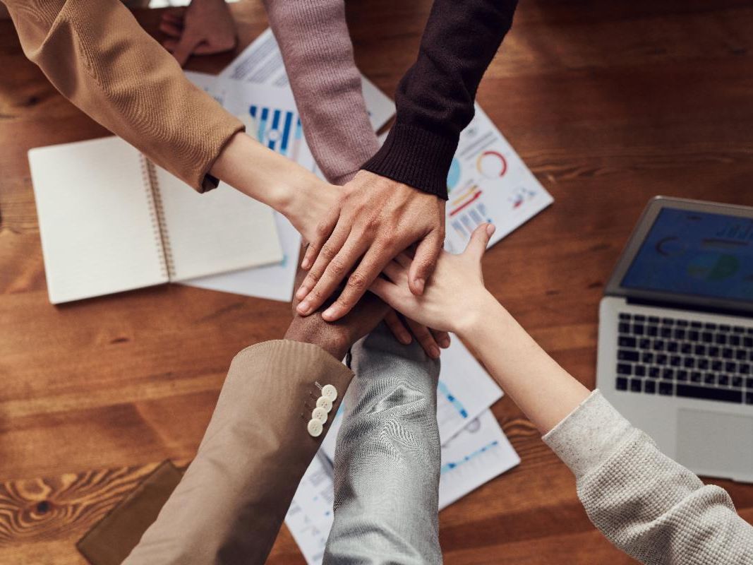 A group of professionals showing unity and teamwork by stacking their hands on a table.