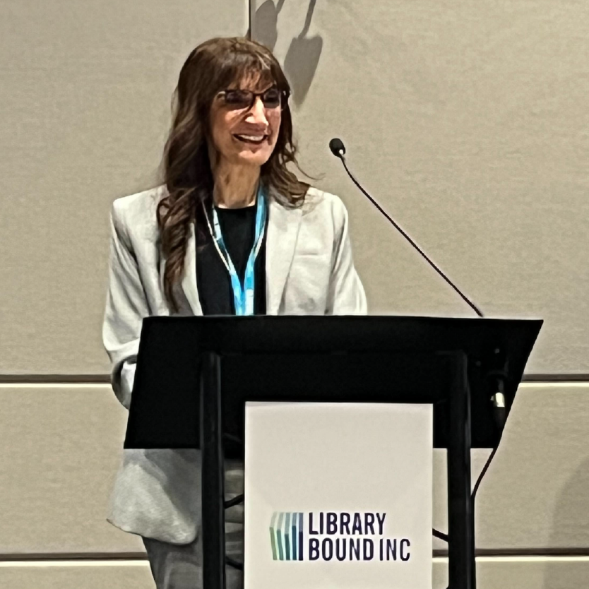 Anita stands at a podium. She has a large smile on her face as she looks into the audience.