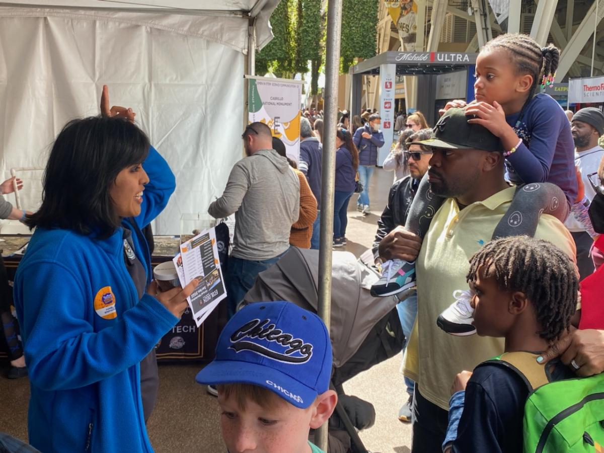 CVA Hannah speaks with a family during the San Diego Festival of Science & Engineering about sea hares, while holding up "bunny ears" with her fingers.