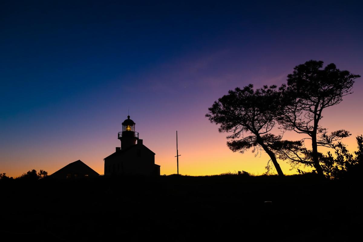 Violet and yellow sunset overlooking the Old Point Loma Lighthouse's silhouette.