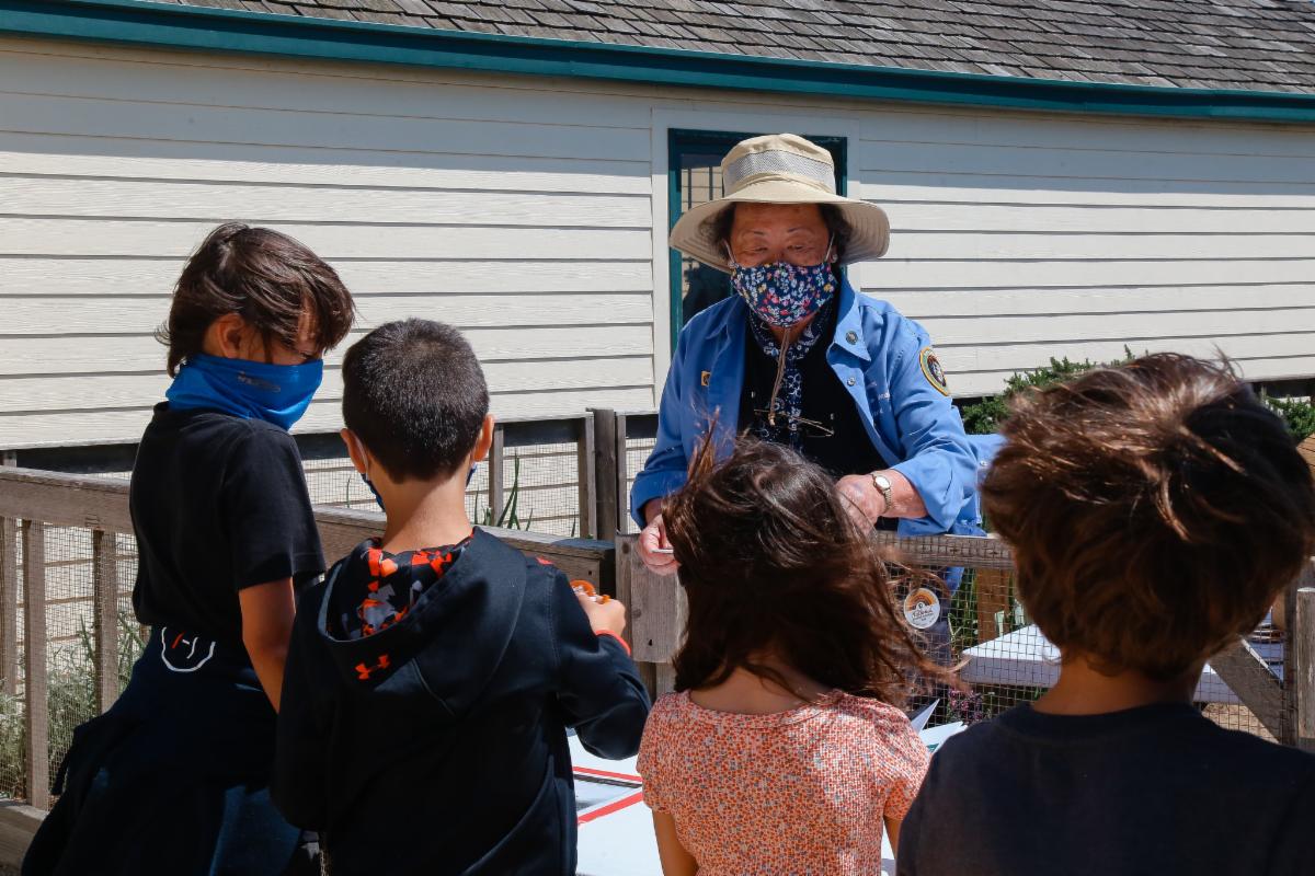 VIP Susie speaks to young children, who are asking questions about the lighthouse's kitchen garden behind her. 