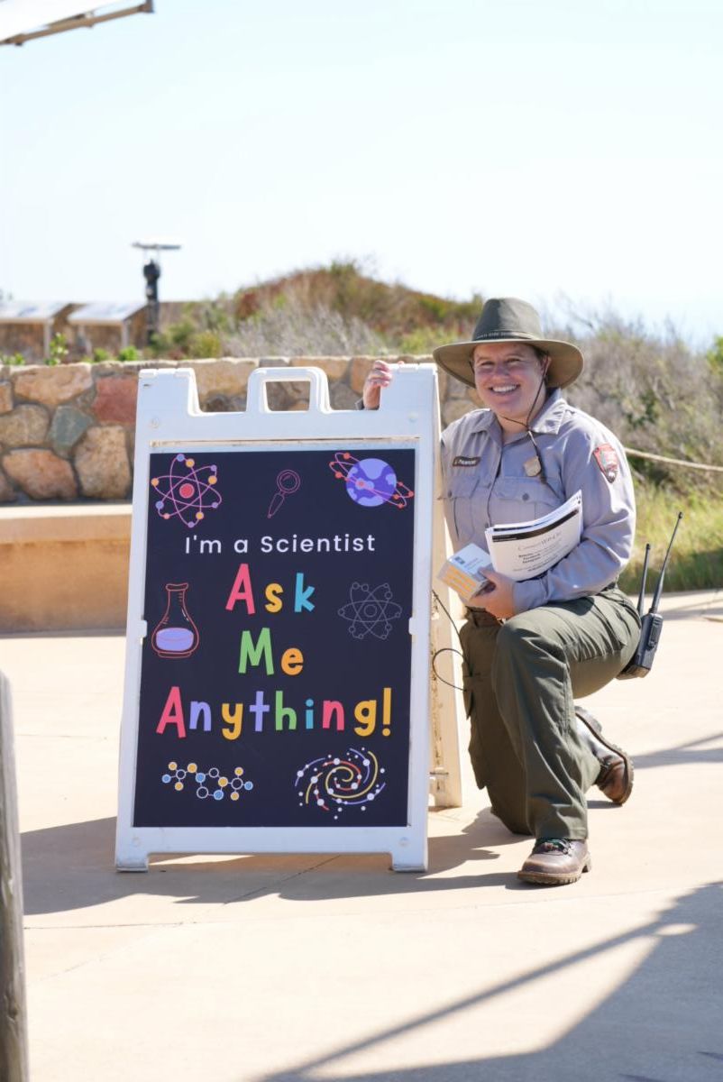 Natural Resources Program Manager, Ranger Lauren, smiles next to a sign reading "Ask me anything! I'm a scientist!" 