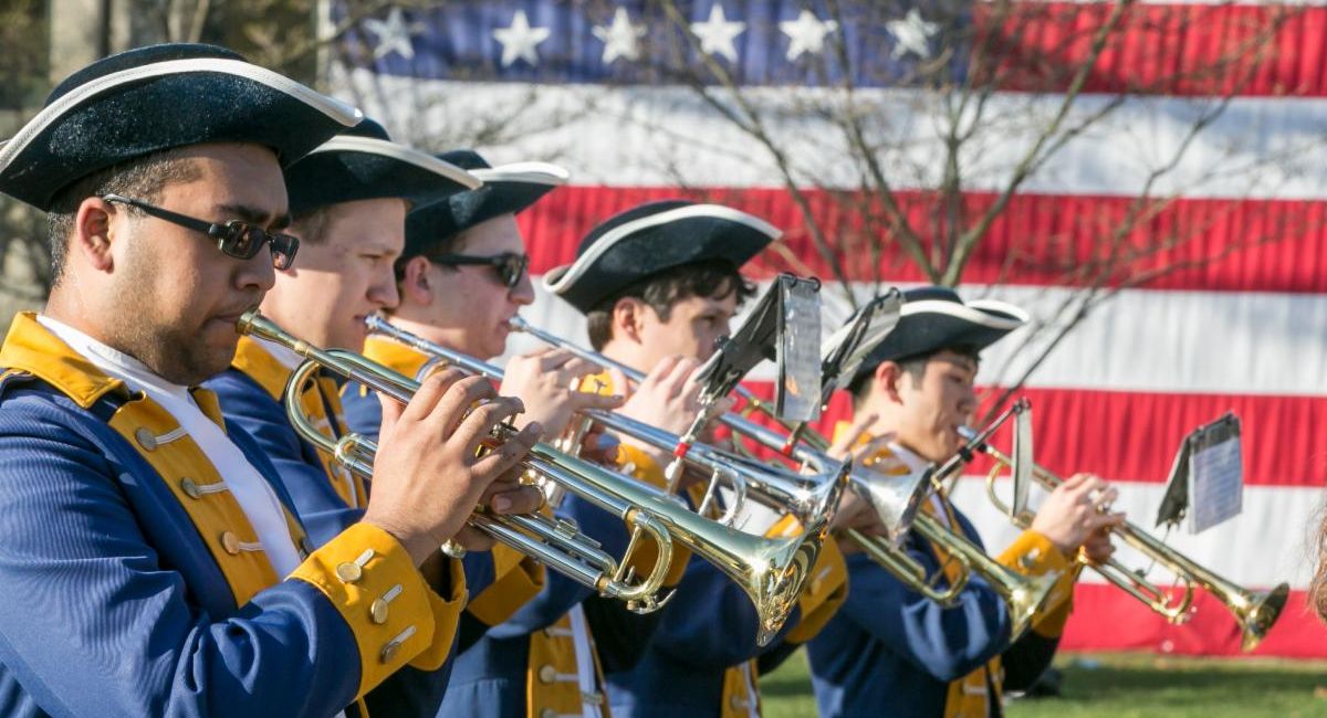 Reenactors playing trumpets in front of an american flag on a past Patriots day