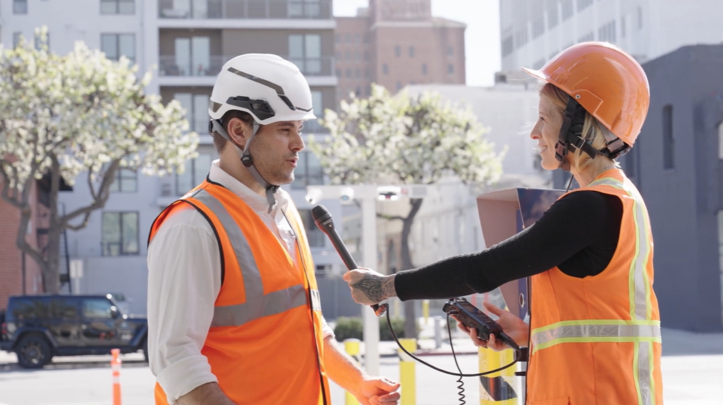 A man being interviewed by a woman in orange construction vests and hard hats
