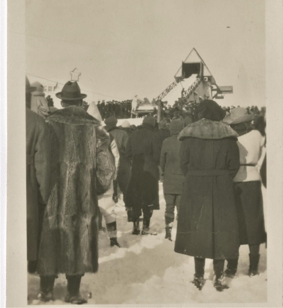 Crowd of people in winter clothing watch a ski jump.