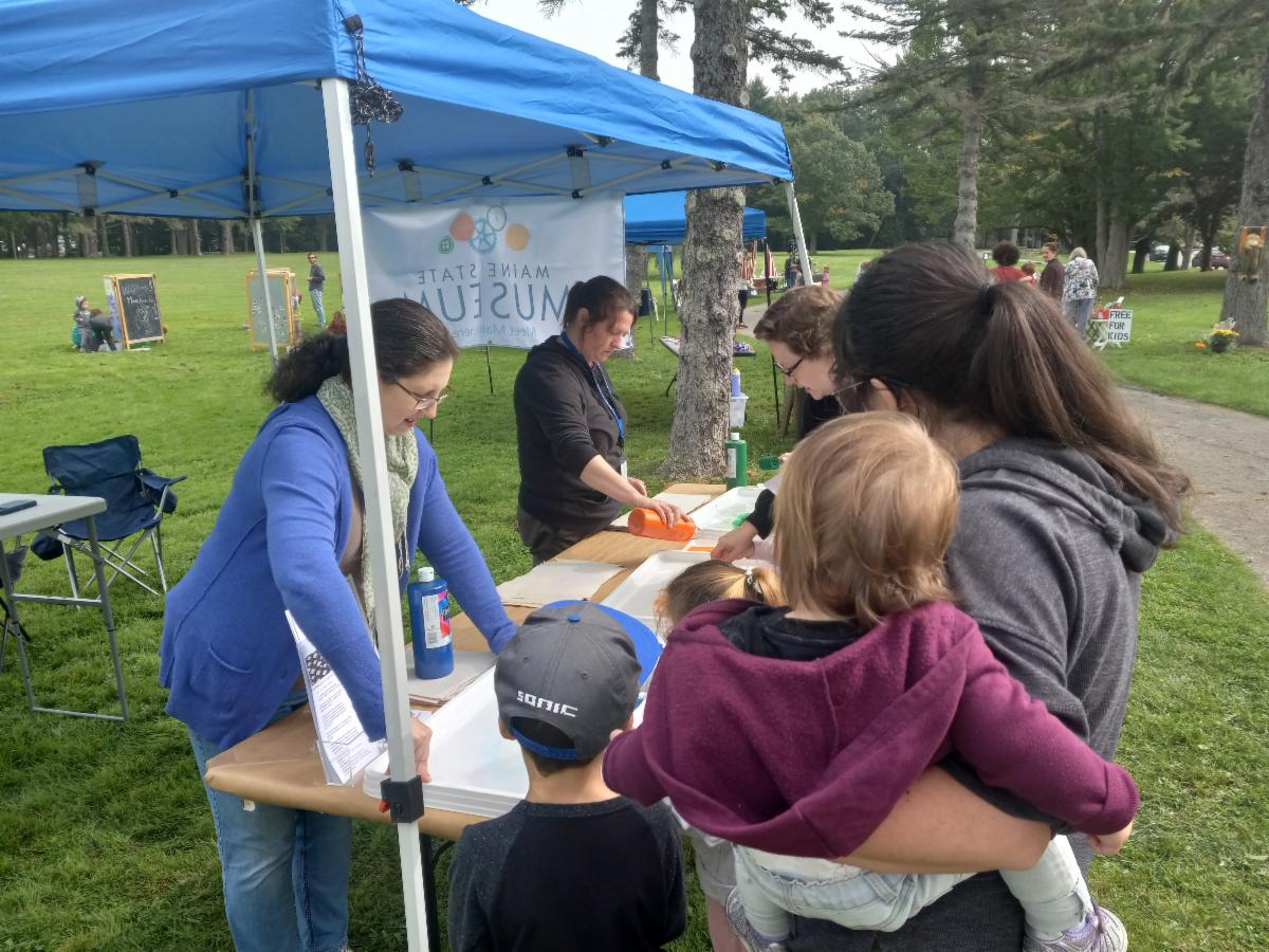 Group of adults and children gathered around a table doing a painting activity.