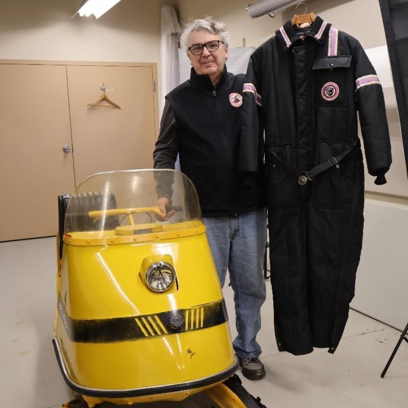 Al Swett of the Maine Snowmobile Association poses with the museum's 1960s Ski-Doo snowmobile and the suit he donated.