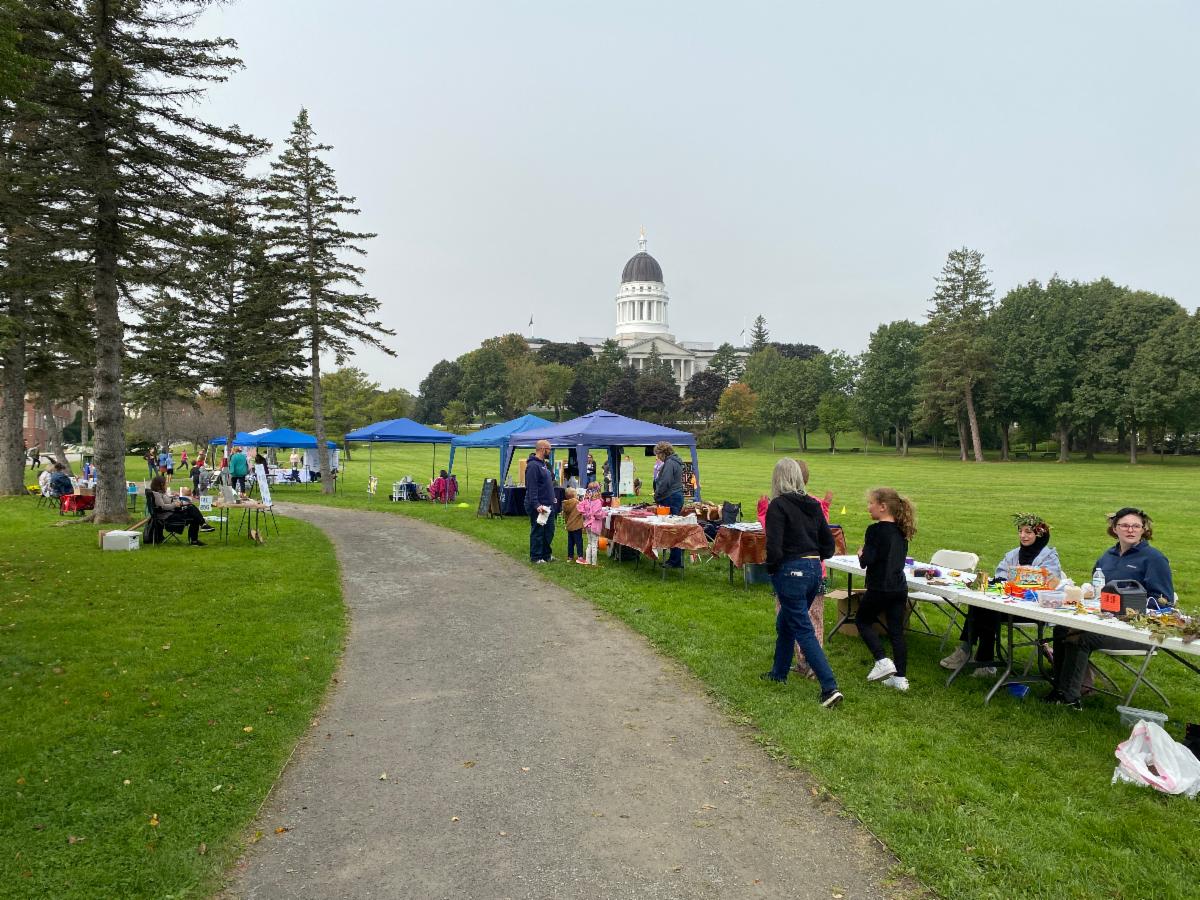 Outdoor scene with tables and tents in front of the Maine State Capitol Building. 