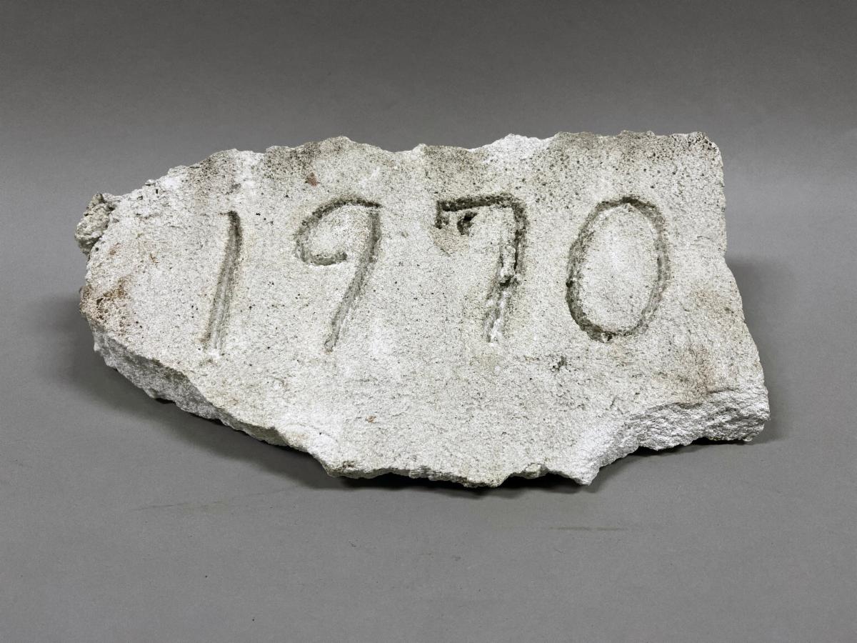 Broken piece of concrete with the date "1970" scratched in it.