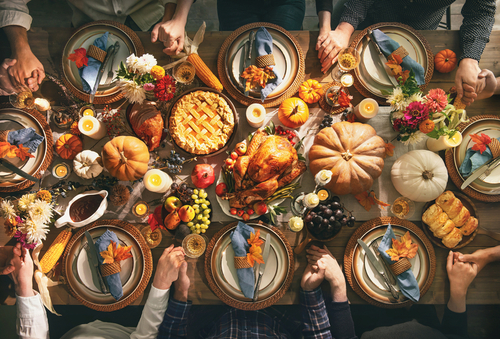 Group of friends or family members giving thanks to God at festive turkey dinner table together. Thanksgiving celebration traditional dinner concept