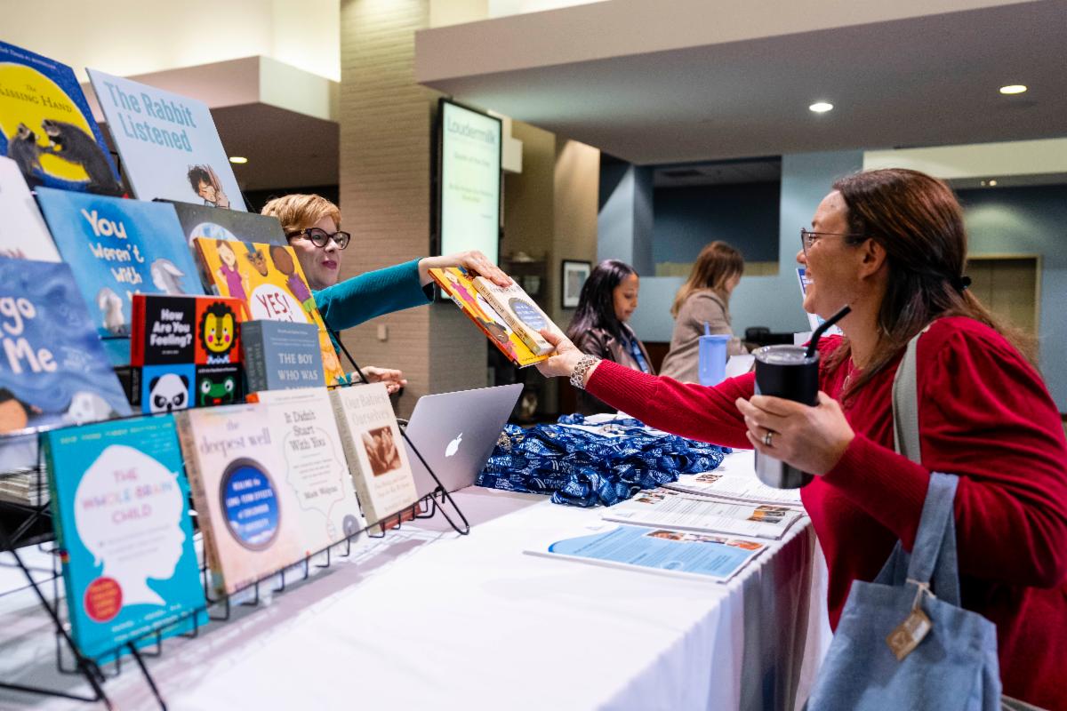 WHite woman from CLD handing a book to a white woman attendee