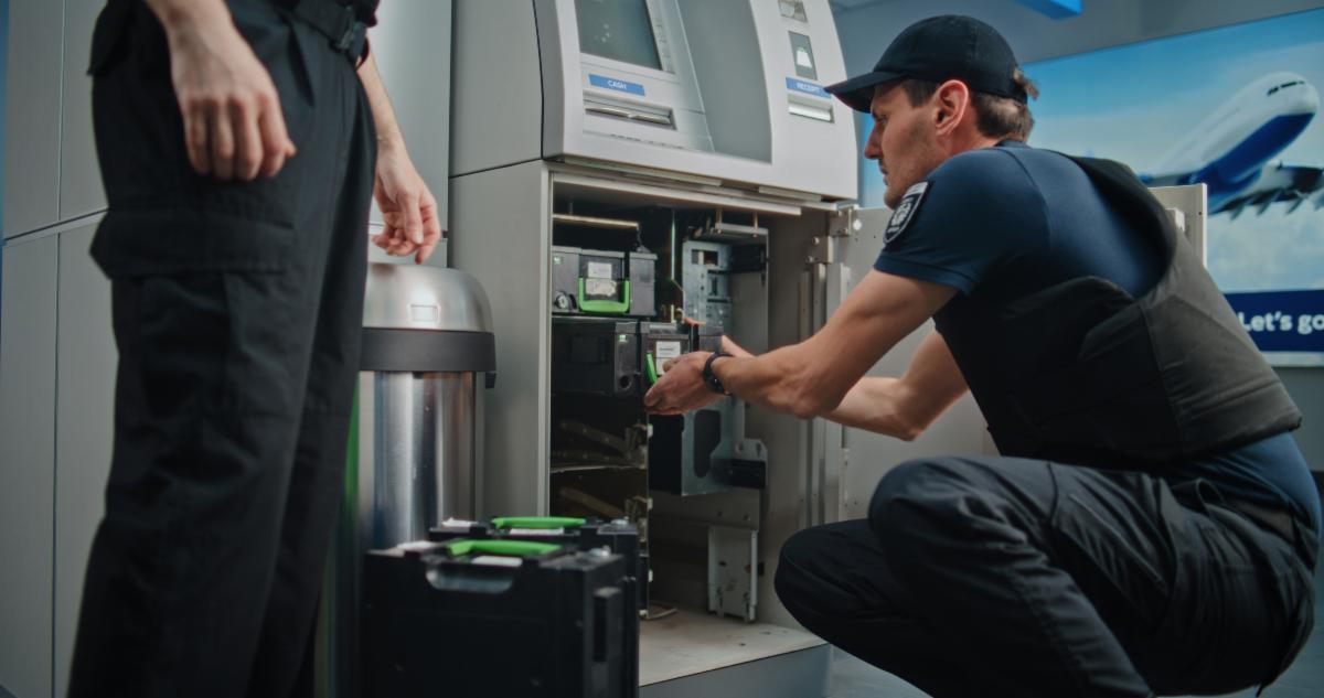 Professional Guards in Uniforms Performing ATM Encashment Procedure in Airport Terminal Changing Cash Cassettes Servicing Cash Machine. Cash-in-transit Operation for Safe Money Transportation.