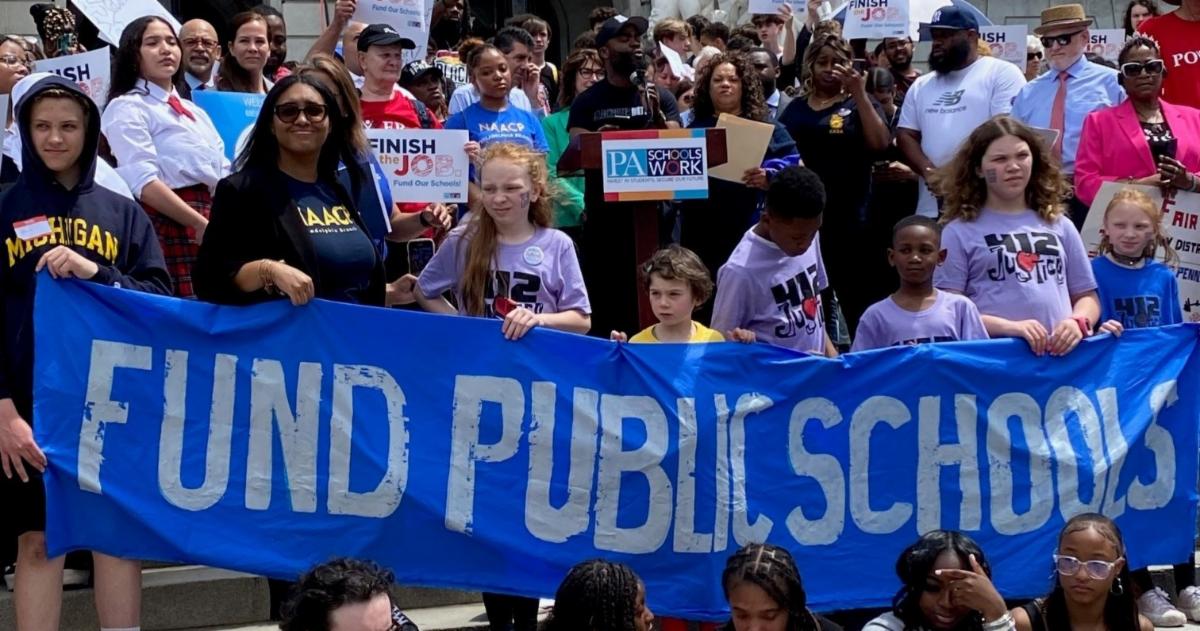 supporters of public schools hold colorful signs at a Harrisburg rally