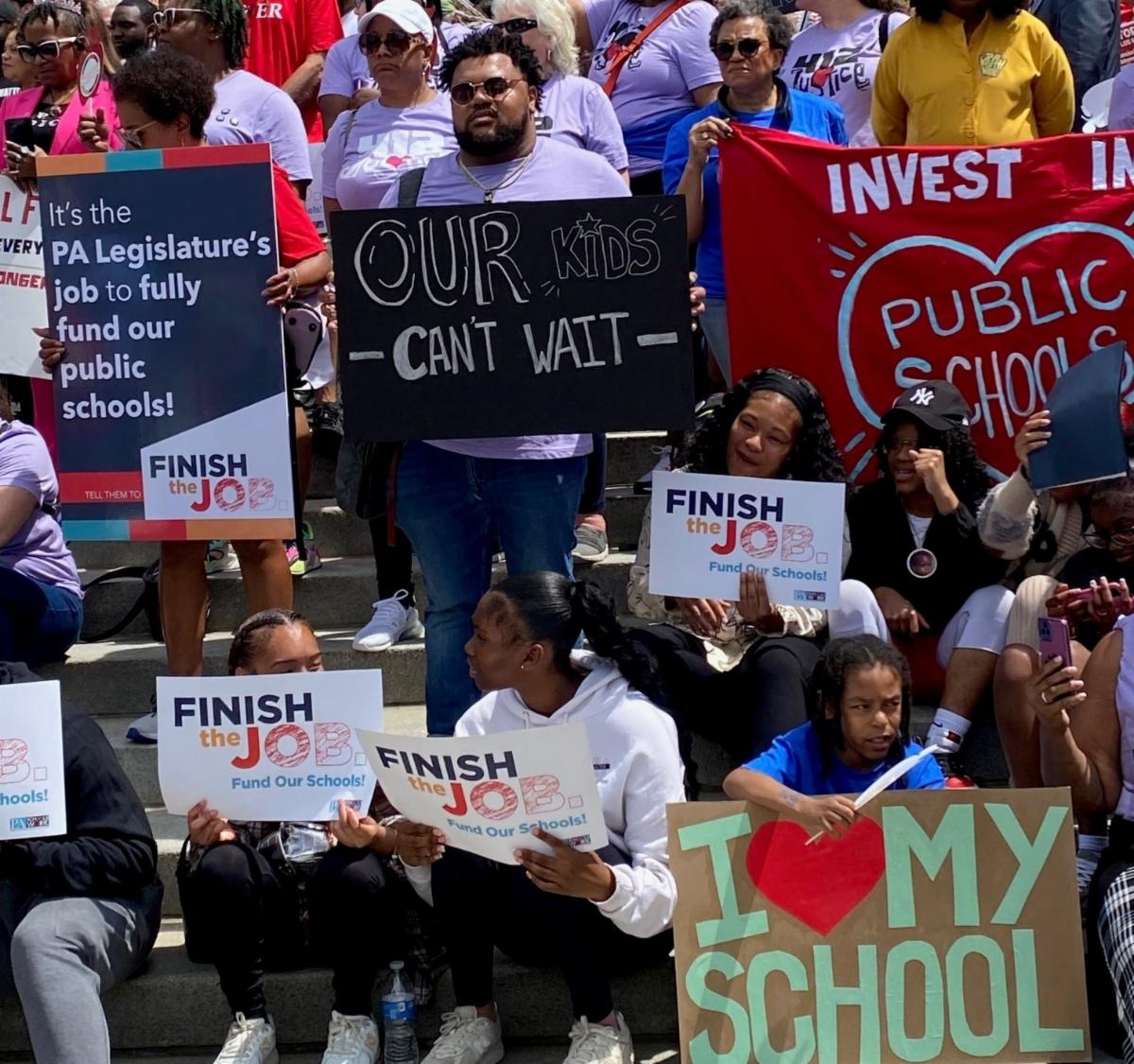 supporters of public schools hold colorful signs at a Harrisburg rally
