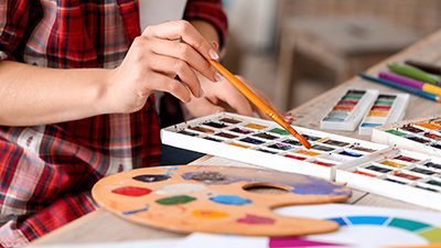 A hand holding a paintbrush with pallettes of paint.