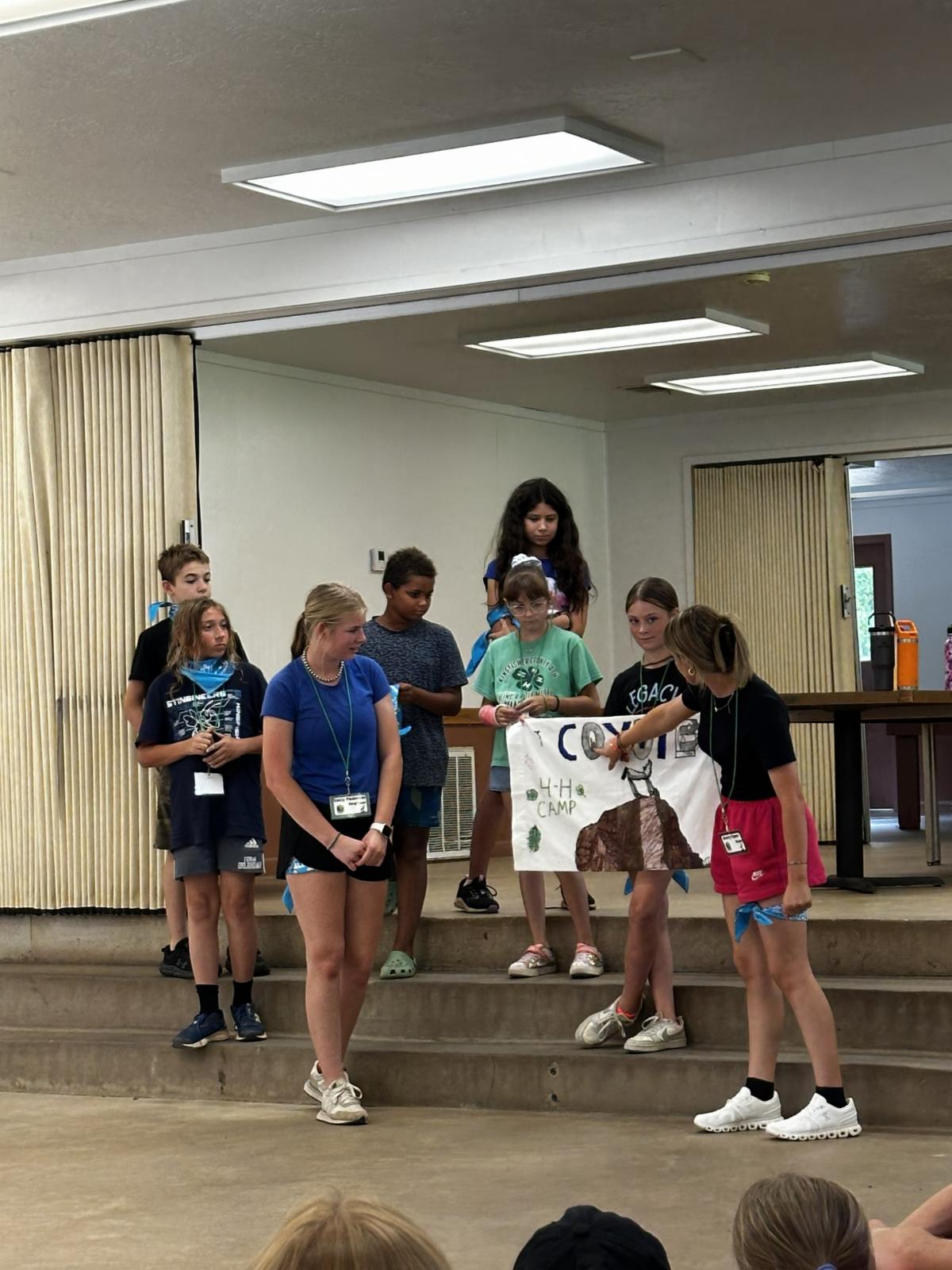 Youth participants present a team poster and camp project on stage during a 4-H camp group activity, showcasing teamwork, creativity, and leadership skills.