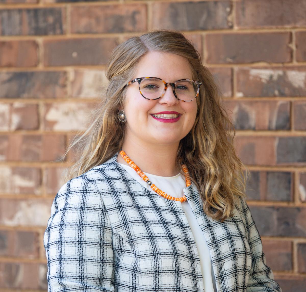 Portrait of Rylee Glazier, Blaine County's Agriculture and 4-H Educator, standing in front of a brick wall.