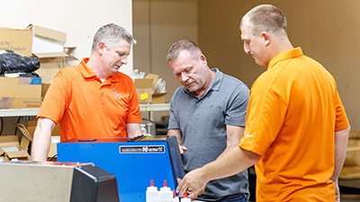 Three men in a shop looking at a piece of machinery that is blue.
