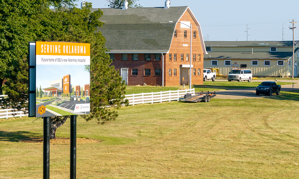 A coming soon Vet Med Teaching Hospital sign with the agronomy research station in the background.