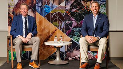 Dr. Jayson Lusk and David Newman sit in front of a photo collage backdrop.