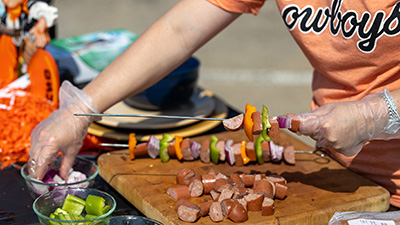 A person putting meat and vegetables on a skewer.