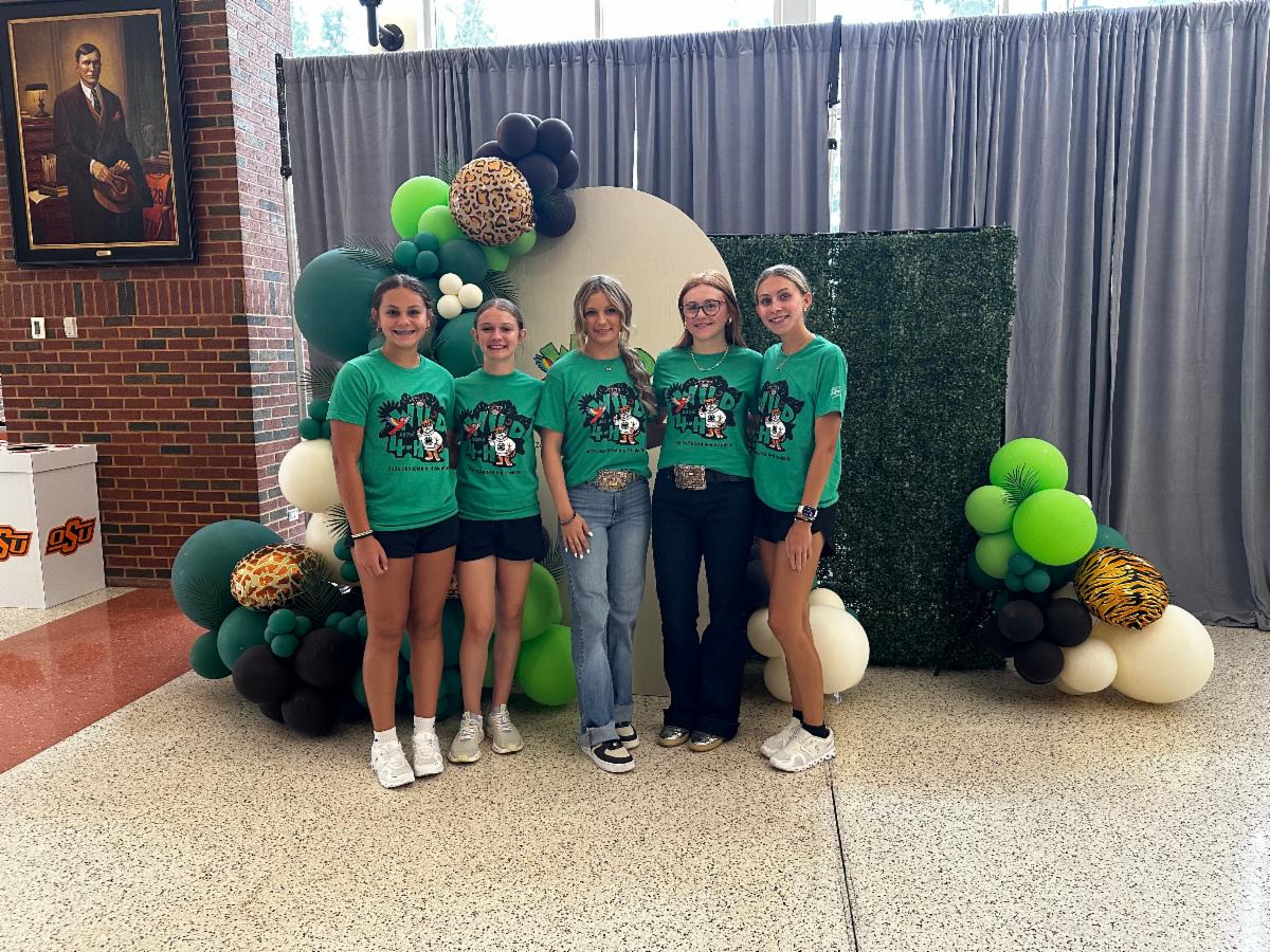 Five 4-H participants pose in matching “Wild About 4-H” shirts in front of a wildlife-themed backdrop with balloon decorations during a 4-H event.