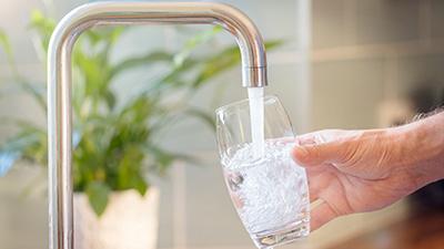 Water flows from a faucet into a drinking glass.