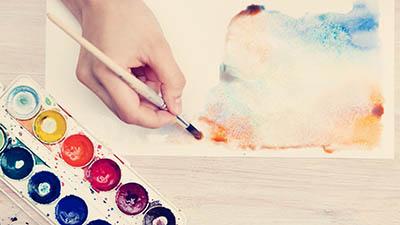 A hand paints with water colors on a white paper.