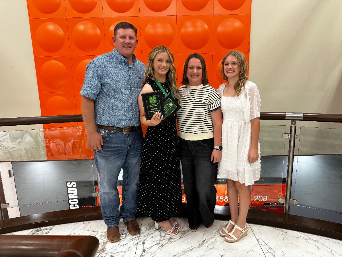 A 4-H participant holding award plaques and a medallion poses with family members at a 4-H recognition event, celebrating achievement, leadership, and involvement in 4-H.