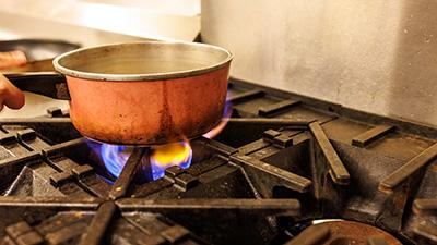 A gas stove flame heads a copper pot.