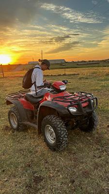 A student worker sits on a 4-wheeler during sunset.