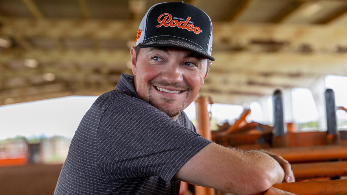 Joby Bush leaning over a fence and smiling back at the camera at the Oklahoma State Rodeo practice arena.