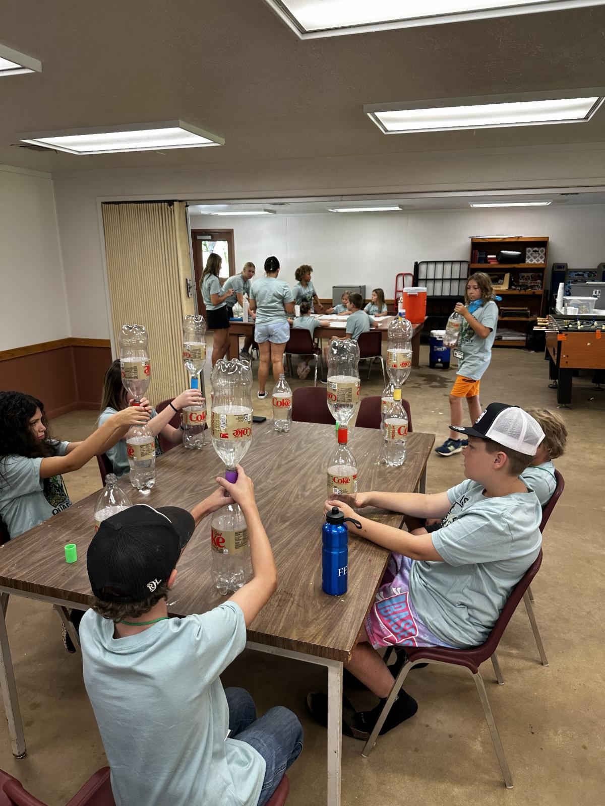 4-H campers work together to balance and stack plastic bottles during a team-building challenge that promotes problem-solving, communication, and teamwork.