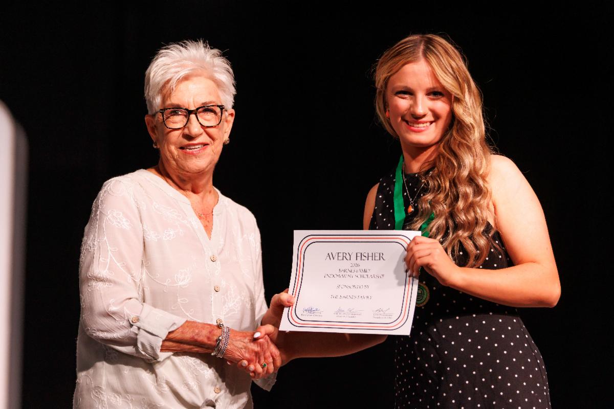 Avery Fisher receives a scholarship award at the 105th Oklahoma 4-H State Roundup. Fisher holds a scholarship certificate while shaking hands with a presenter on stage.