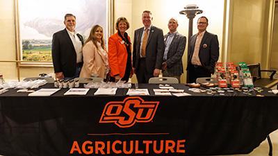A group of people stand behind an OSU Agriculture table.