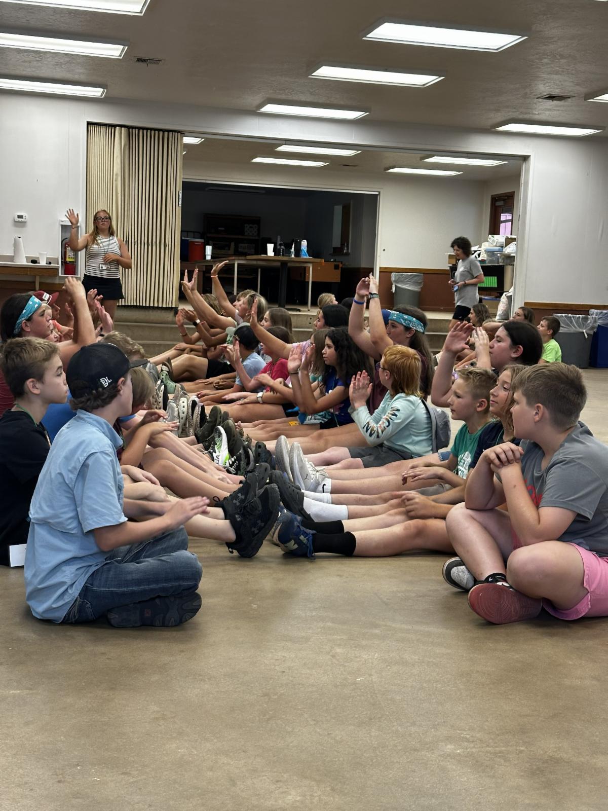 4-H campers take part in a group team-building activity, sitting in rows and interacting with one another during a fun camp leadership and communication exercise.