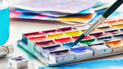 A paintbrush is dipped in a watercolor palette.
