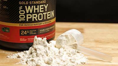 A spilled scoop of vanilla protein powder sits next to the product container.