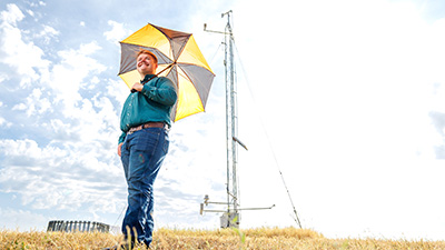 Aaron Long holds an umbrella next to a Mesonet tower.