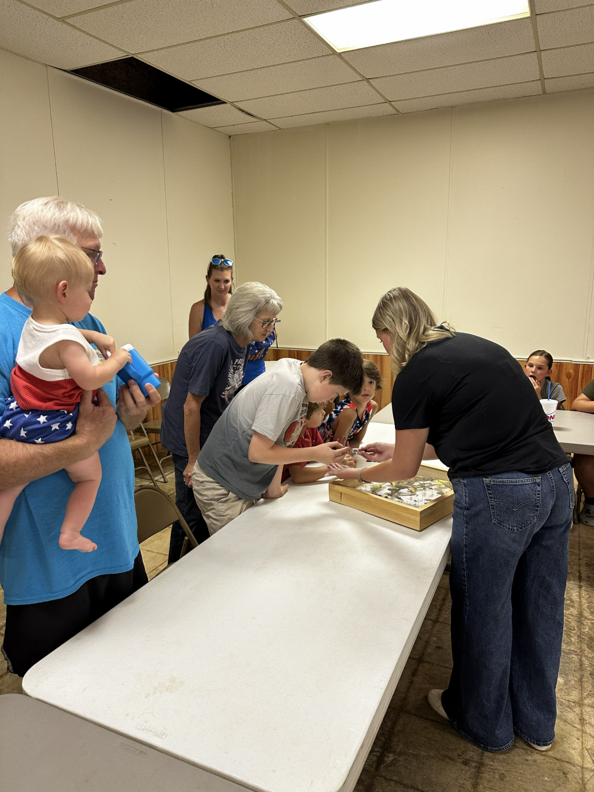 Youth and adults participate in a hands-on 4-H science activity, examining insect specimens and learning about entomology through an interactive educational demonstration.