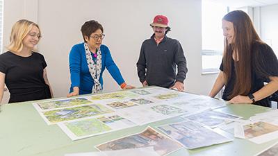 Three students and an instructor look over a printed plan for landscape architecture.