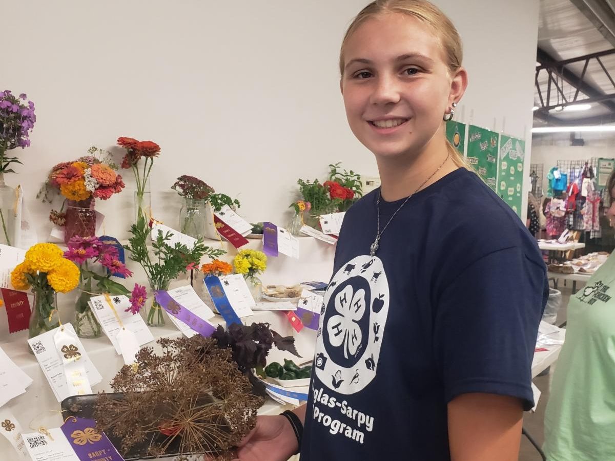 teen girl holding herbs standing in front of flowers and herbs at county fair 